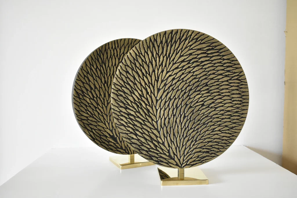 deux petites oeuvres rondes de diamètre 30 cm en laiton et écailles de plâtre sculptées sont photographiées en atelier sur fond blanc avant livraison. Les oeuvres sont constituées de petites écailles teintées de tons bronze et doré en surface. Le socle est en laiton poli miroir.