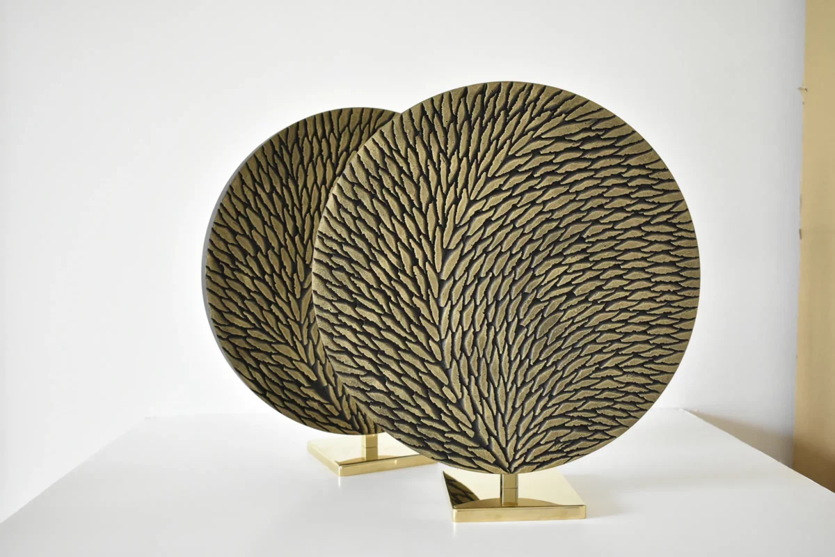 deux petites oeuvres rondes de diamètre 30 cm en laiton et écailles de plâtre sculptées sont photographiées en atelier sur fond blanc avant livraison. Les oeuvres sont constituées de petites écailles teintées de tons bronze et doré en surface. Le socle est en laiton poli miroir.