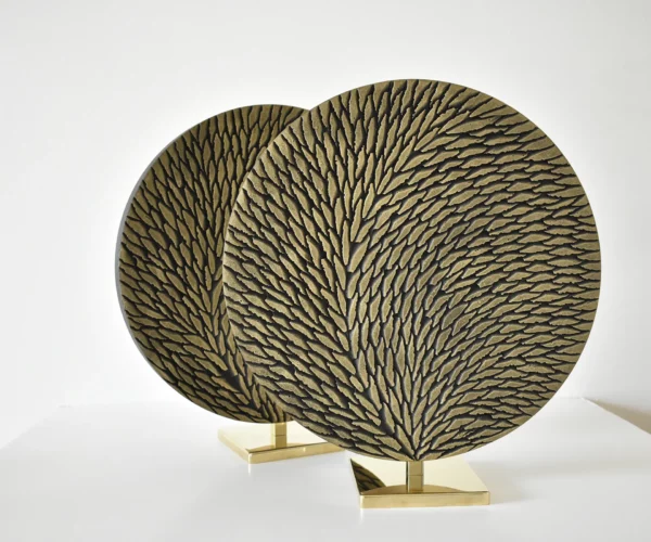 deux petites oeuvres rondes de diamètre 30 cm en laiton et écailles de plâtre sculptées sont photographiées en atelier sur fond blanc avant livraison. Les oeuvres sont constituées de petites écailles teintées de tons bronze et doré en surface. Le socle est en laiton poli miroir.