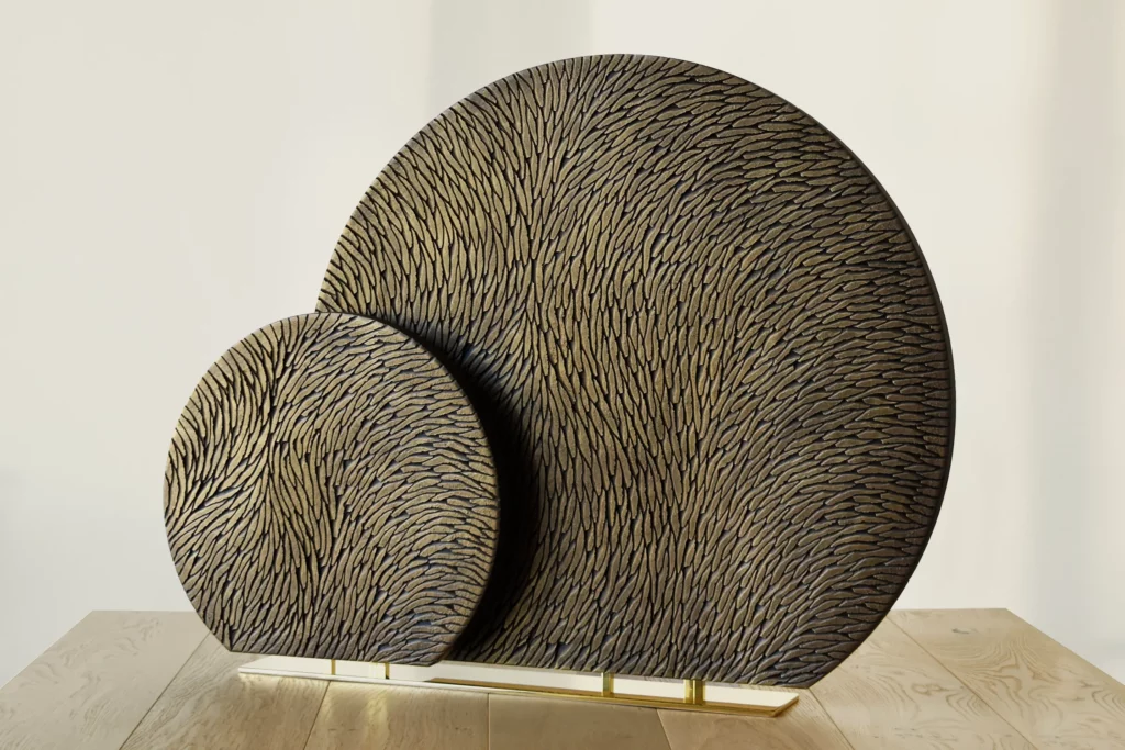 Vue de face d'une sculpture double sur un même socle en laiton poli miroir. Les deux sculptures sont des cercles tronqués de diamètre différents. Elles sont toutes les 2 en plâtre sculpté patiné bronze doré.