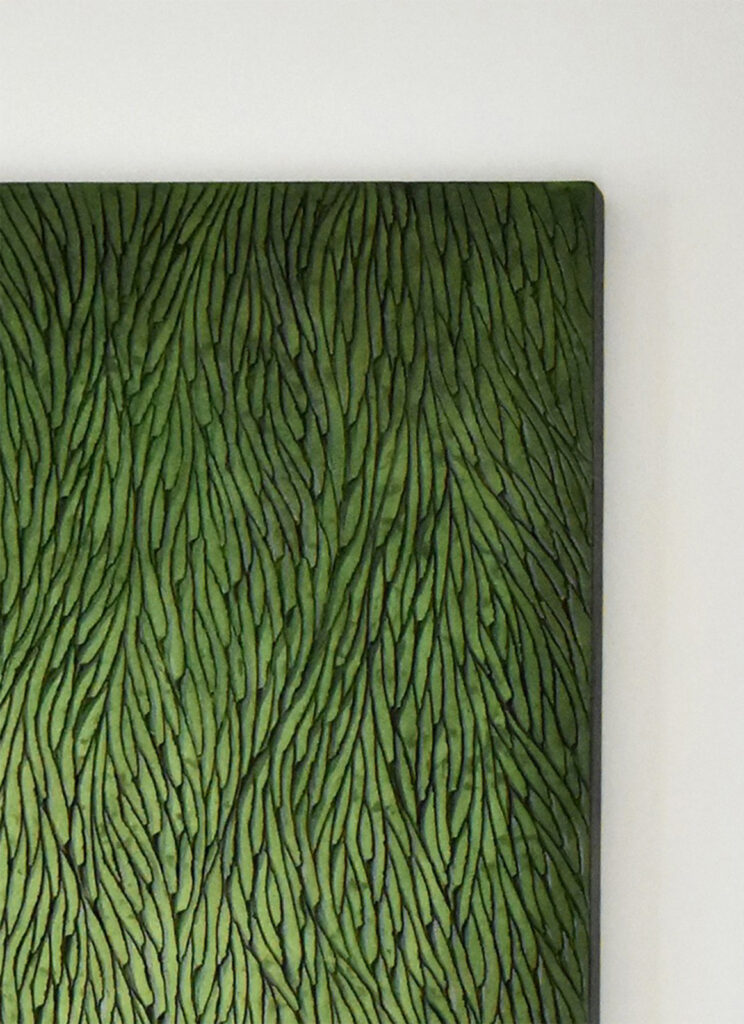 Accroché au mur blanc type galerie, on voit l'angle d'une sculpture murale, un détail de matière sculptée, des écailles de plâtre méticuleusement agencées selon un graphisme d'inspiration végétale. L'oeuvre est teintée de nuances de verts, on retrouve plusieurs pigments travaillés en dilution, qui crée un dégradé, tout en conservant la luminosité de l'oeuvre.