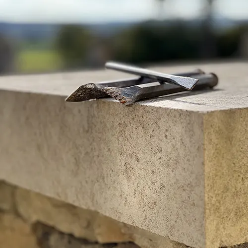 En extérieur, des outils de taille de pierre, gradine et burin plat, sont posé sur une pierre de Bourgogne.