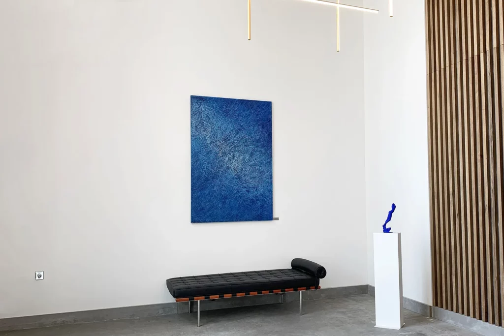 Grand hall d'accueil d'un entreprise lyonnaise, grand mur blanc, mobilier épuré, au mur, une oeuvre murale de l'artiste sculpteur Mylène Mai. Ici un format vertical, de grande dimension, en écailles de plâtre sculptées, patinées aux teintes de bleus, en dégréadés doux et lumineux