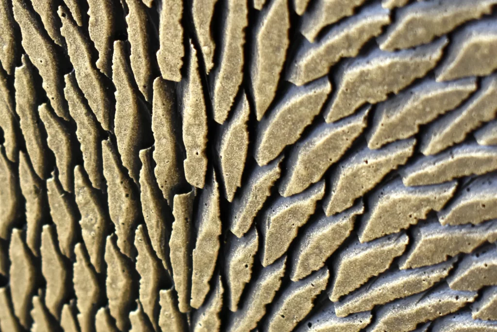 Zoom sur des très petites écailles de plâtre sculptées et teintées de bronze et de doré en surface.