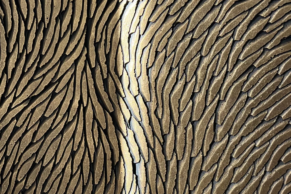 Zoom sur une sculpture sur socle en plâtre constituée de multiples écailles. La patine de cette œuvre d'art sur mesure est dans des tons bronze, brun, doré.