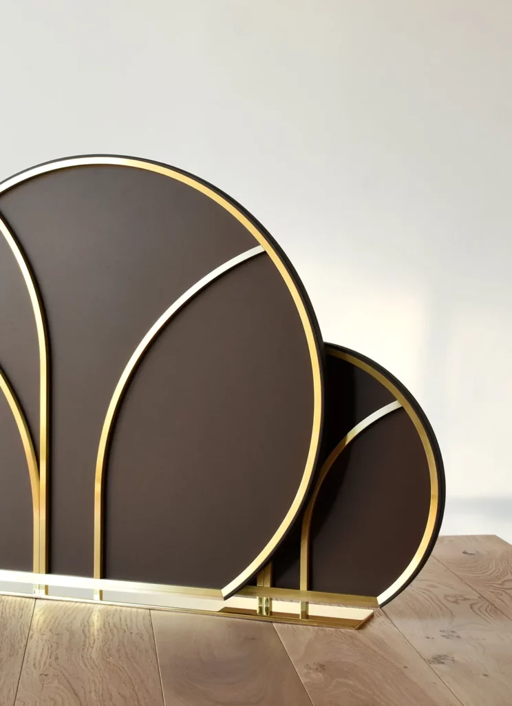 Le dos de cette sculpture double sur socle est réalisé en laiton cintré, parfaitement assemblé. L'œuvre a une forme est d'inspiration art déco, un cercle tronqué avec des ramures cintrées. Cette pièce sur mesure fait appel aux savoir-faire et à l'excellence des métiers d'art.