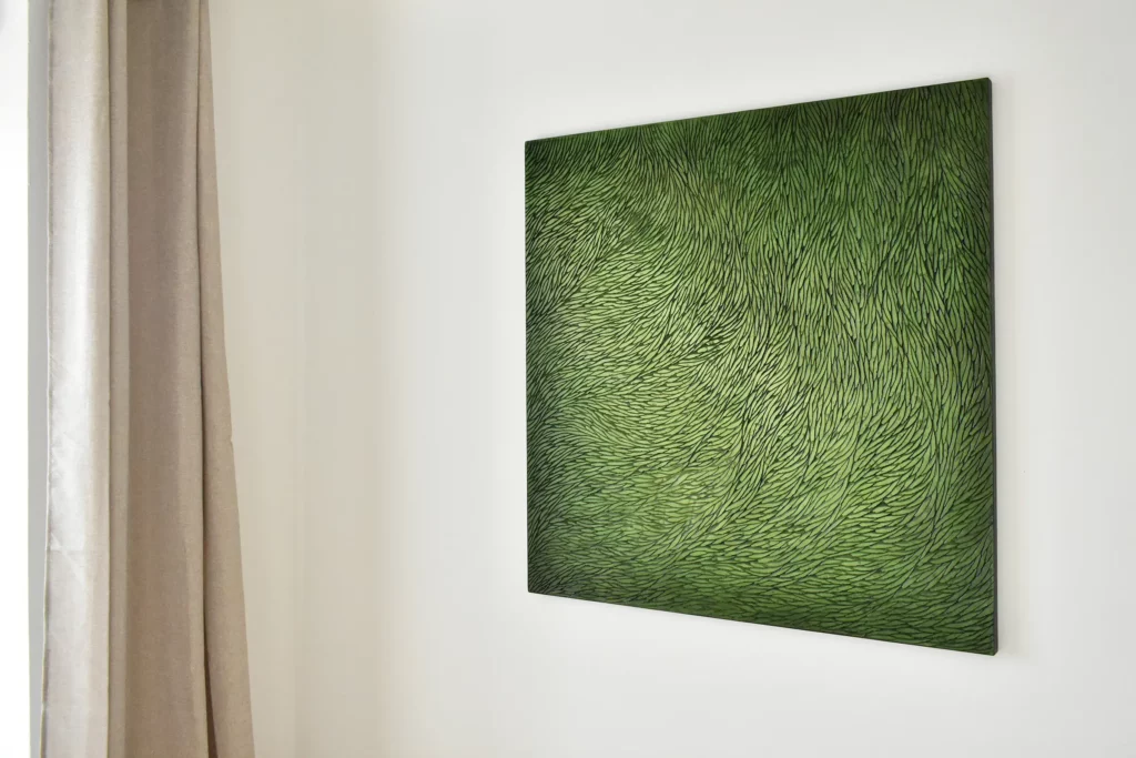 Dans un intérieur aux tons neutres type galerie d'art, murs blancs et rideaux beige, est installé au mur une sculpture murale de format carré, en plâtre sculpté de l'atelier Mylène Mai. L'artiste contemporaine a sculpté l'entière surface de l'œuvre d'écailles de plâtre, puis les a teinté, patiné de nuances de verts avec des pigments naturels, qui donnent de magnifiques dégradés de couleur et une luminosité à cette oeuvre.