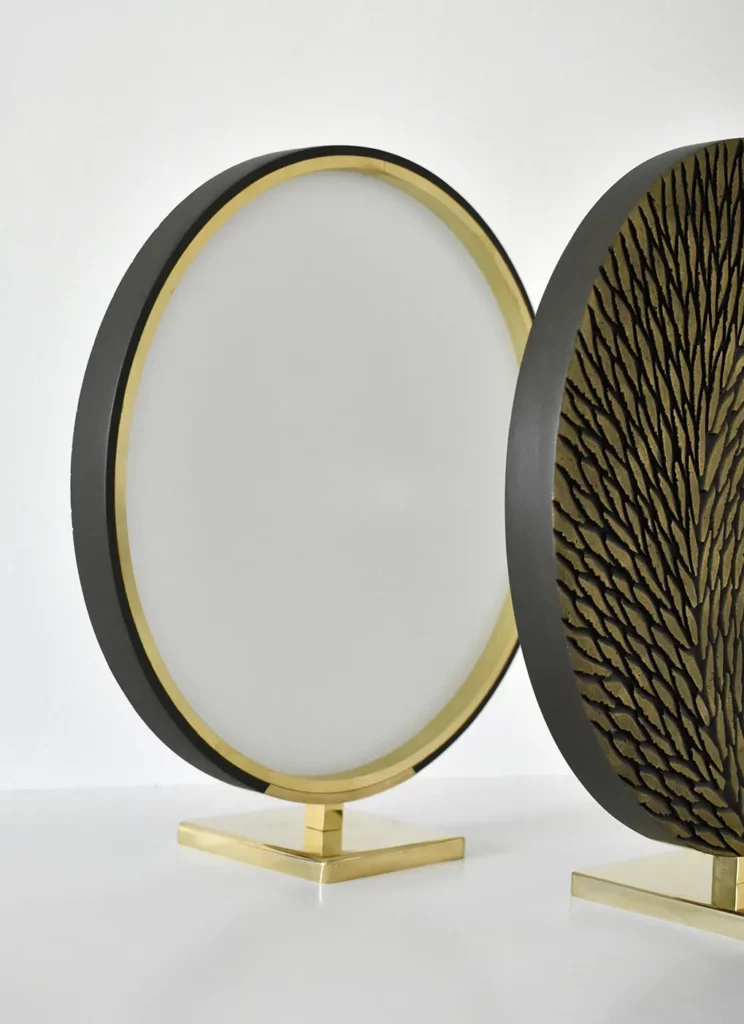 2 petites oeuvres sur socle sont photographiées sur fond blanc, l'une de face partiellement visibles, ornée d'écailles de plâtre sculptées et patinées en bronze doré; l'autre de dos, révèle la structure en laiton. Les socles sont en laiton poli miroir.