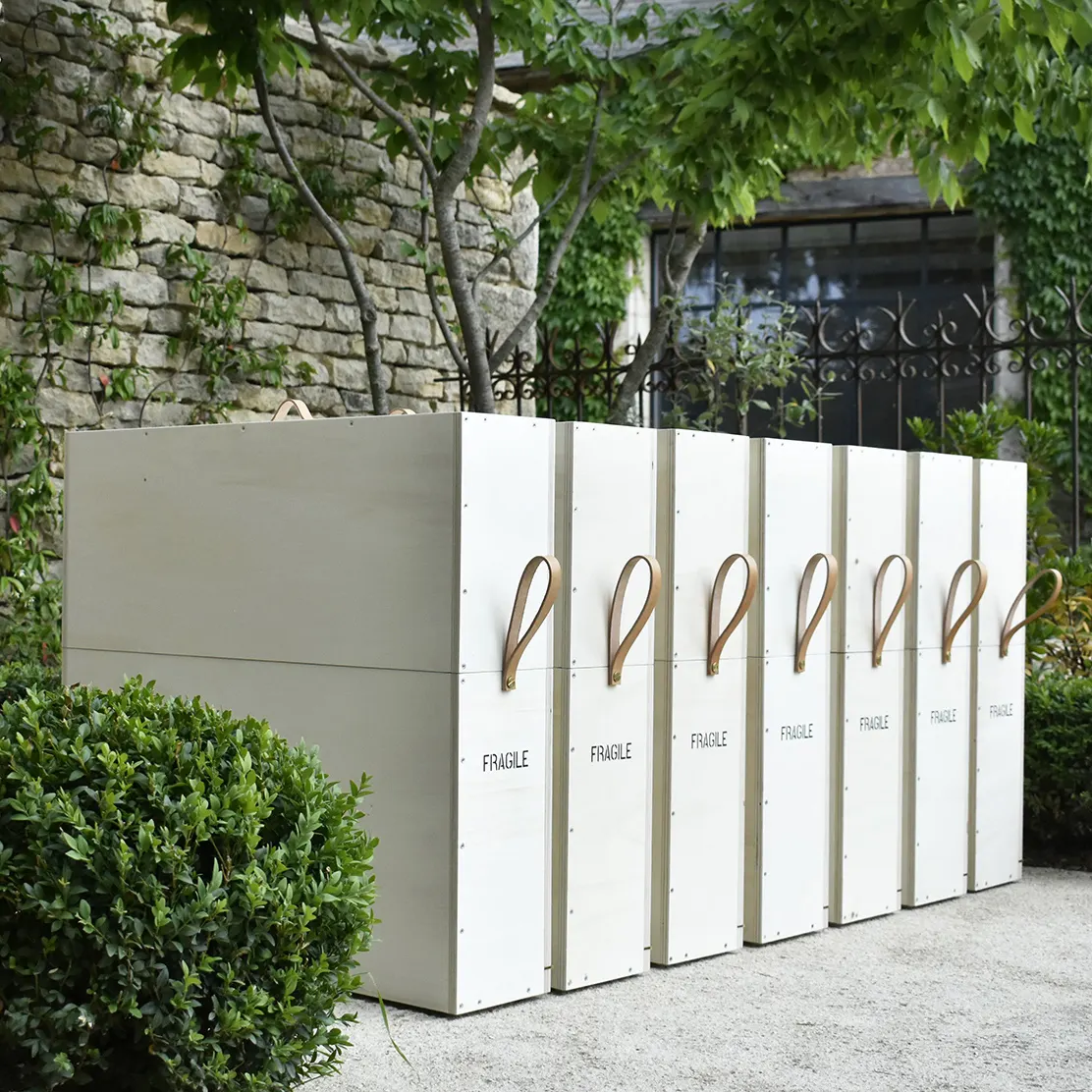 Dans le jardin de l'atelier Mylène Mai en Bourgogne, fait de mur de pierre et planté de buis, sont disposées 7 caisses en bois laiton et cuir. Ces caisses transportent une commande d'exception de 7 œuvres sur mesure pour la maison Cartier