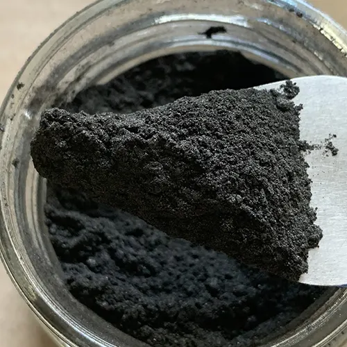 Vue de dessus, un pot de pigment gris ouvert à l'atelier de Mylène Mai, une spatule prélève des pigments pour le travail de patine des oeuvres.