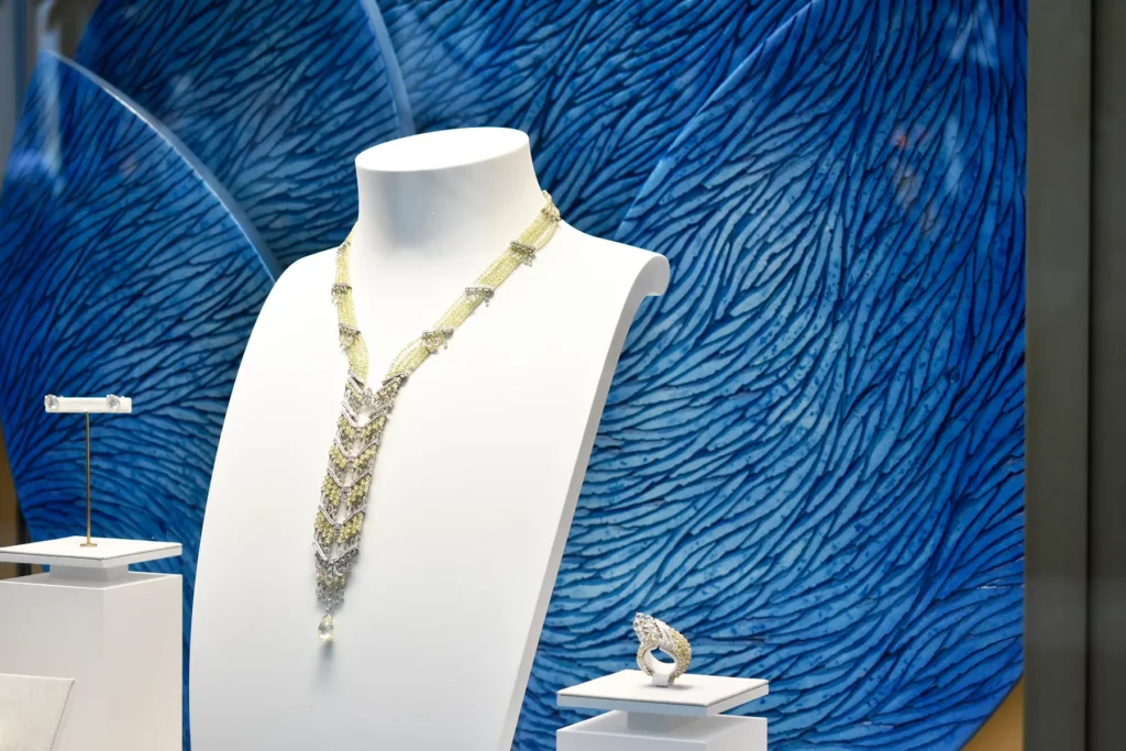 Dans une vitrine de la maison Cartier à Monaco, une oeuvre de l'atelier Mylène Mai, de forme ronde et constituée de plusieurs plans sert de décor et d'écrin à une parure de haute joaillerie. L'oeuvre sur mesure est en relief, constituée de multiples écailles sculptées, teintées de pigments bleus en dégradés.