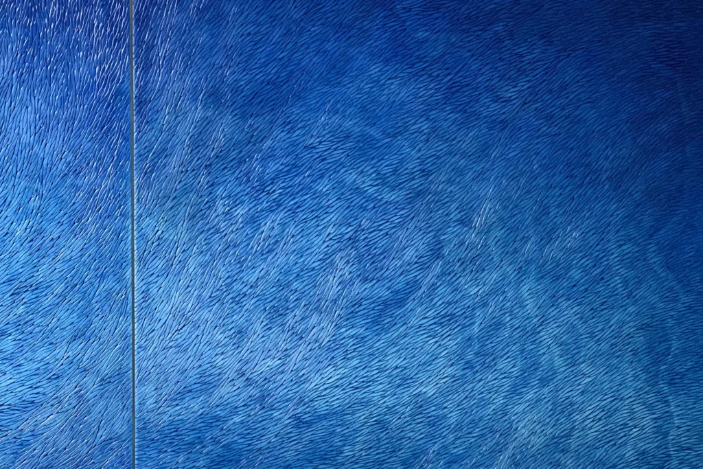 Une vue de face d'un grand triptyque bleu, la vue est zoomée sur seulement 2 parties de l'oeuvre de grande dimension. Les écailles de plâtre bleues se poursuivent d'une pièce à l'autre dans un mouvement fluide et organique.