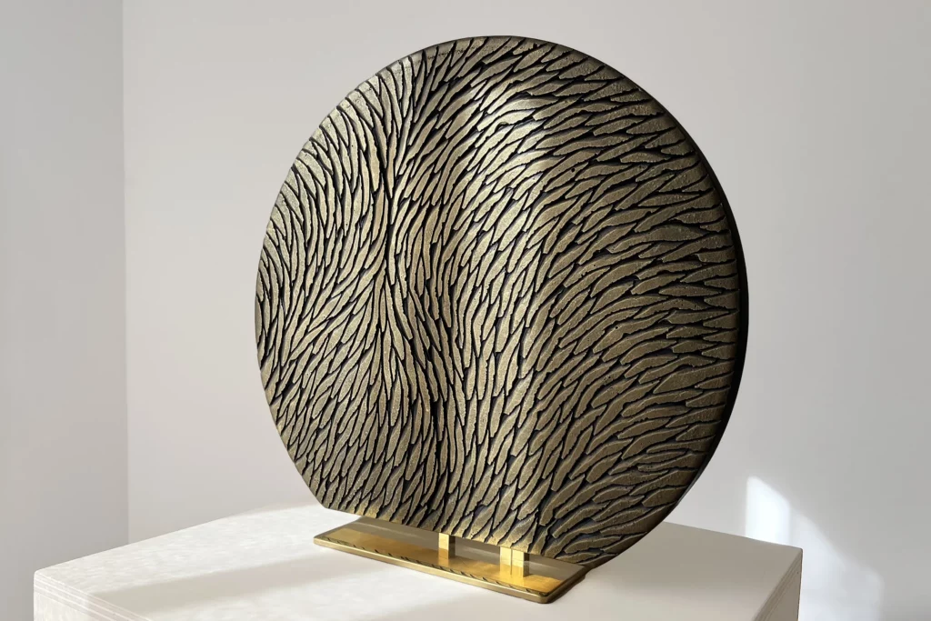 Vue de trois quart d'une sculpture à poser, sur socle, en plâtre et laiton. Une oeuvre en relief, constituée d'écailles de plâtre sculptées, aux couleurs bronze et doré. Un objet d'art luxueux et raffiné.