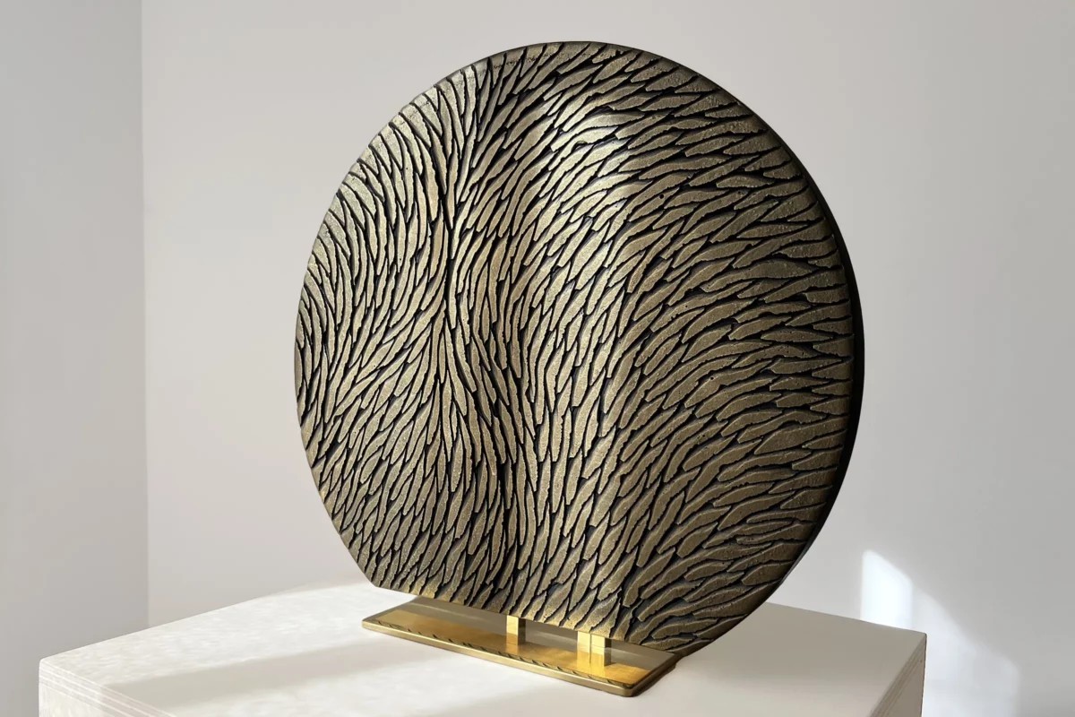 Vue de trois quart d'une sculpture à poser, sur socle, en plâtre et laiton. Une oeuvre en relief, constituée d'écailles de plâtre sculptées, aux couleurs bronze et doré. Un objet d'art luxueux et raffiné.