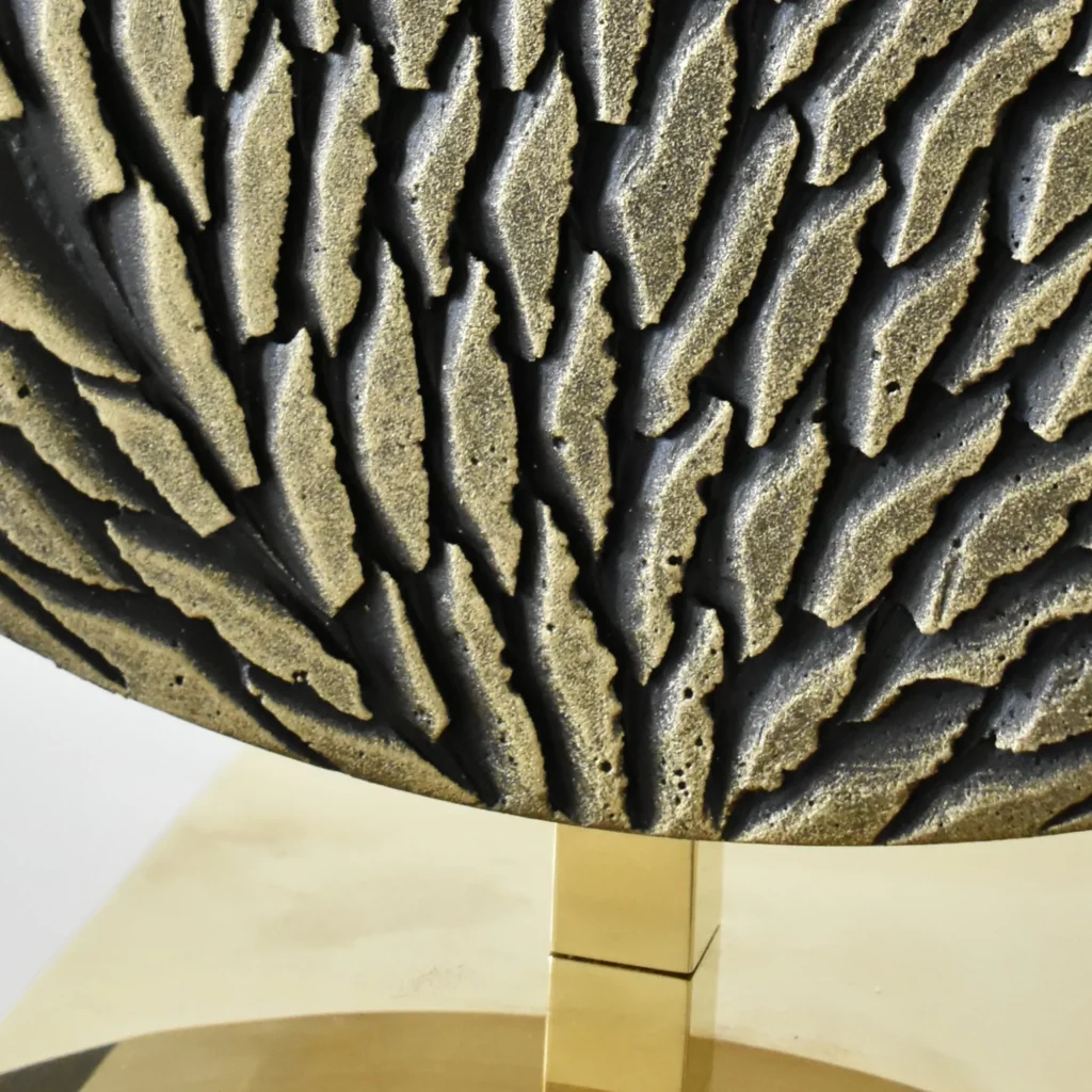 Zoom sur la base d'une oeuvre de l'atelier Mylène Mai. Une oeuvre ronde, de petit format, constitué de petites écailles de plâtre sculptées à la main, patinées et dorées, ainsi que le socle en poli miroir.