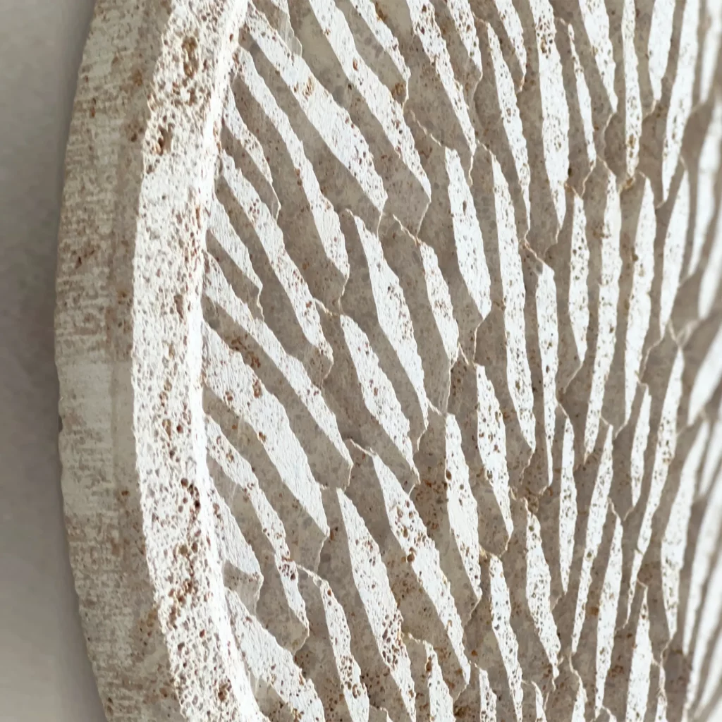 Zoom de trois quart sur une oeuvre murale en écailles de pierre sculptées. La pierre de Bourgogne est beige clair, homogène, les écailles parfaitement maîtrisées ornent la totalité de la surface de l'œuvre.