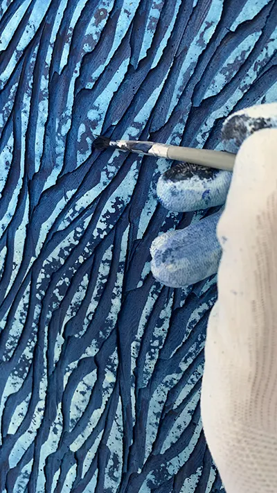 L'artiste Mylène Mai, effectue quelques finitions de teintes au pinceau fin sur une sculpture murale en plâtre.