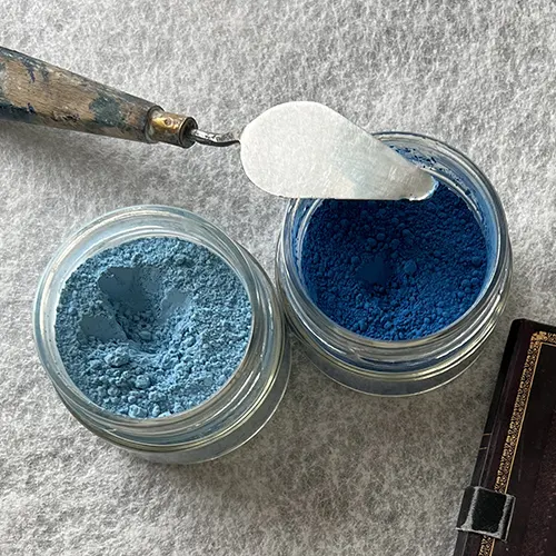 A l'atelier Mylène Mai, sur un plan de travail, deux pots de pigments bleus ouvert, prêts à être utilisées pour la patine d'une sculpture murale sur mesure.