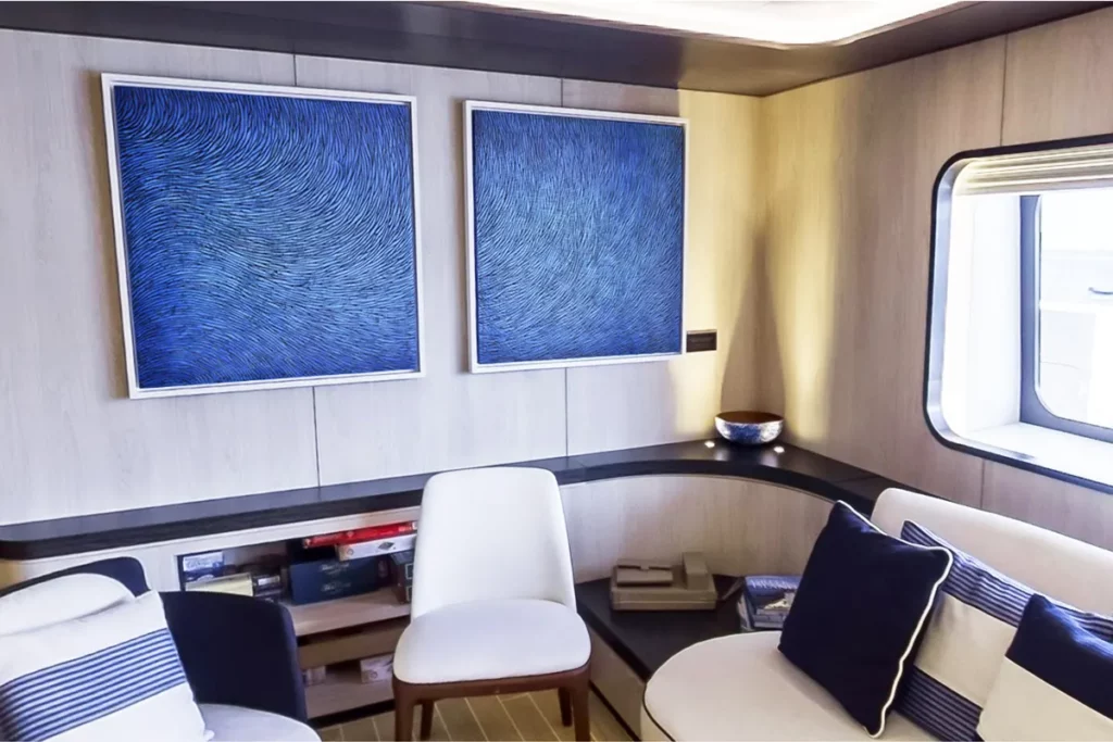 Vue depuis le salon d'accueil du voilier Ponant, quelques sièges, au mur un diptyque de l'artiste Mylène Mai. Ces oeuvres murales sont en écailles de plâtre sculptées, patinées de pigments bleus.