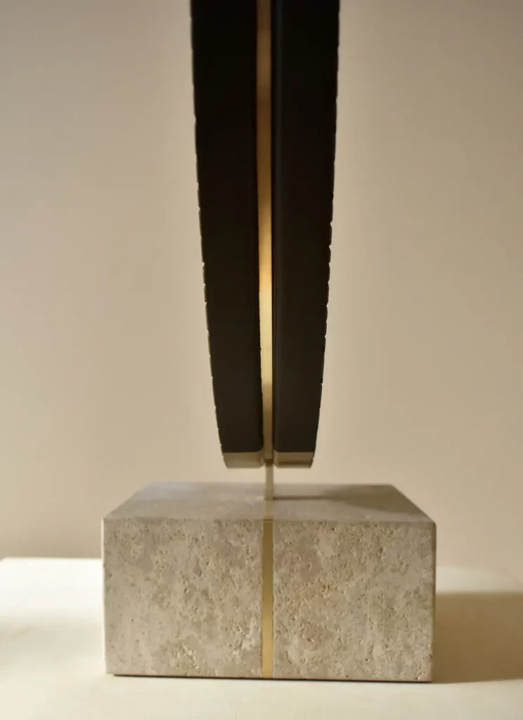 Vue de profil d'une sculpture sur socle de l'atelier Mylène Mai. Les matières de cette oeuvre sur mesure sont la pierre, le laiton, le plâtre sculpté.