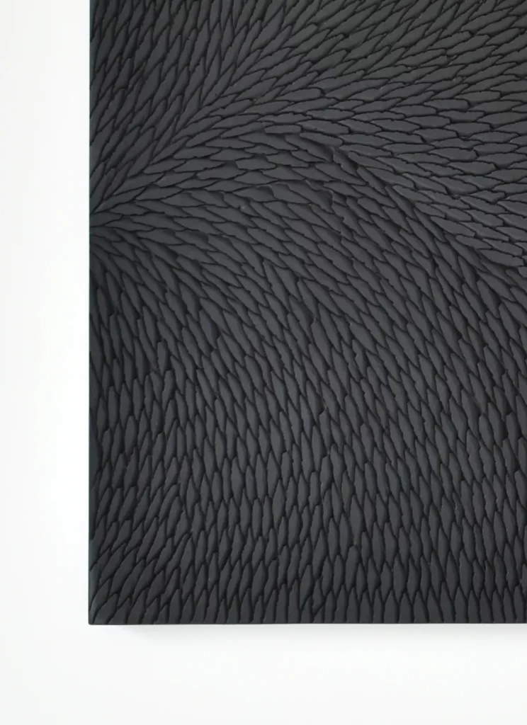 Détail vu de face d'une sculpture murale composée de petites écailles de plâtre noir et gris mat, au mur de l'atelier Mylène Mai