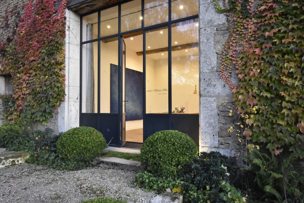 La porte de la verrière de l'atelier en Bourgogne et on aperçoit une oeuvre exposée sur le mur intérieur.