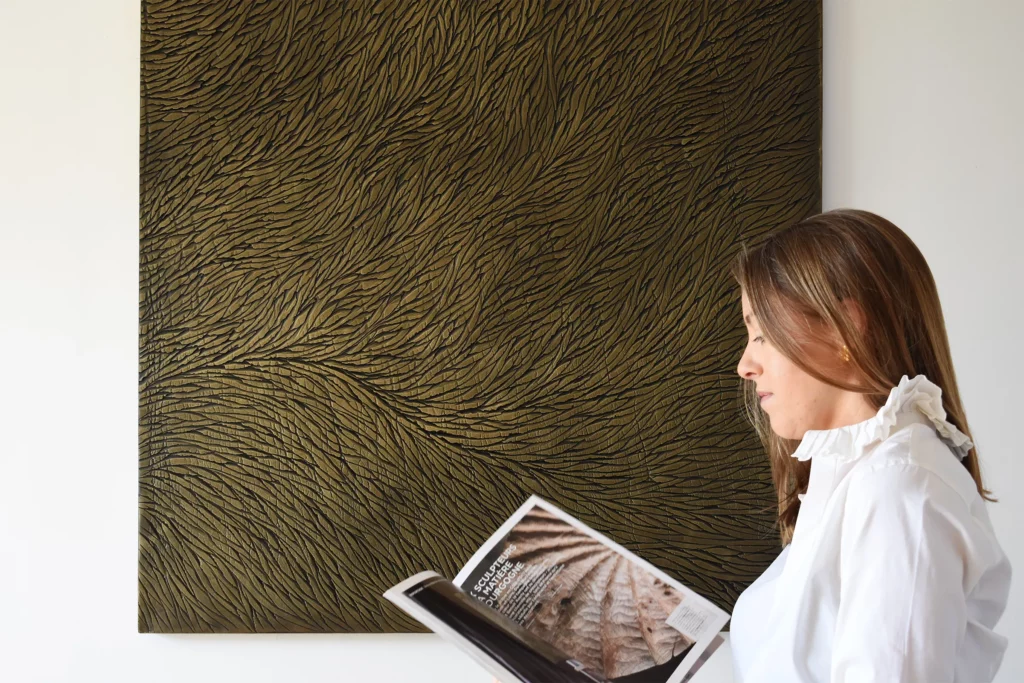 L'artiste sculpteur Mylène Mai regarde un magazine des métiers d'art qui met à l'honneur son atelier et celui d'un autre artiste de Bourgogne. Elle est devant une de ses oeuvres, une sculpture murale en plâtre aux teintes de bronze et réhaussé d'éclats de dorure.