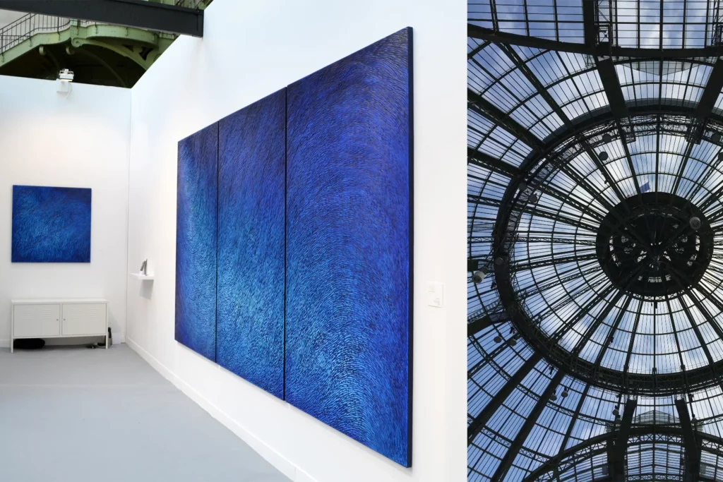 Le stand de l'atelier Mylène Mai lors du salon Révélations 2019, le salon international des métiers d'art au Grand Palais. Est exposé un triptyque bleu mural, de très grand format, cette oeuvre unique monumentale est une sculpture murale en écailles de plâtre, patinées de différents tons de bleus. L'exposition se déroule sous la coupole de la verrière du Grand Palais.